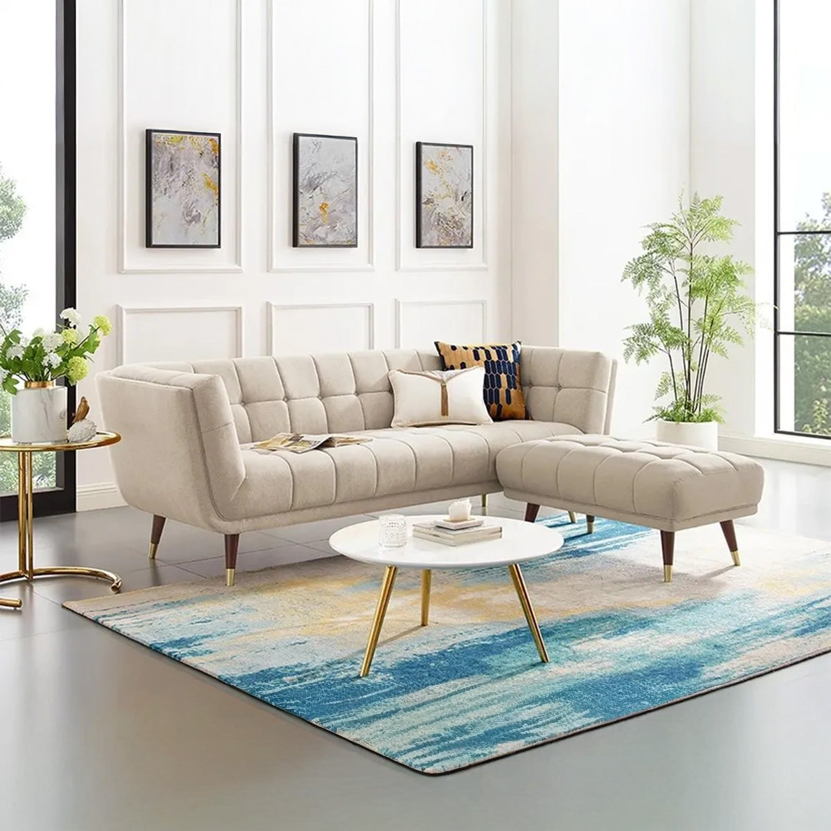 Contemporary living room with a light beige tufted sofa and separate ottoman, featuring a round white coffee table with gold legs and a blue and yellow abstract area rug.