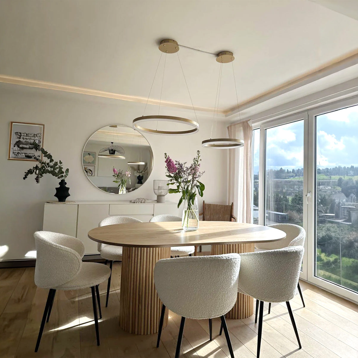 Oval wood dining table with slatted base and six white boucle dining chairs in a modern, sunlit room.