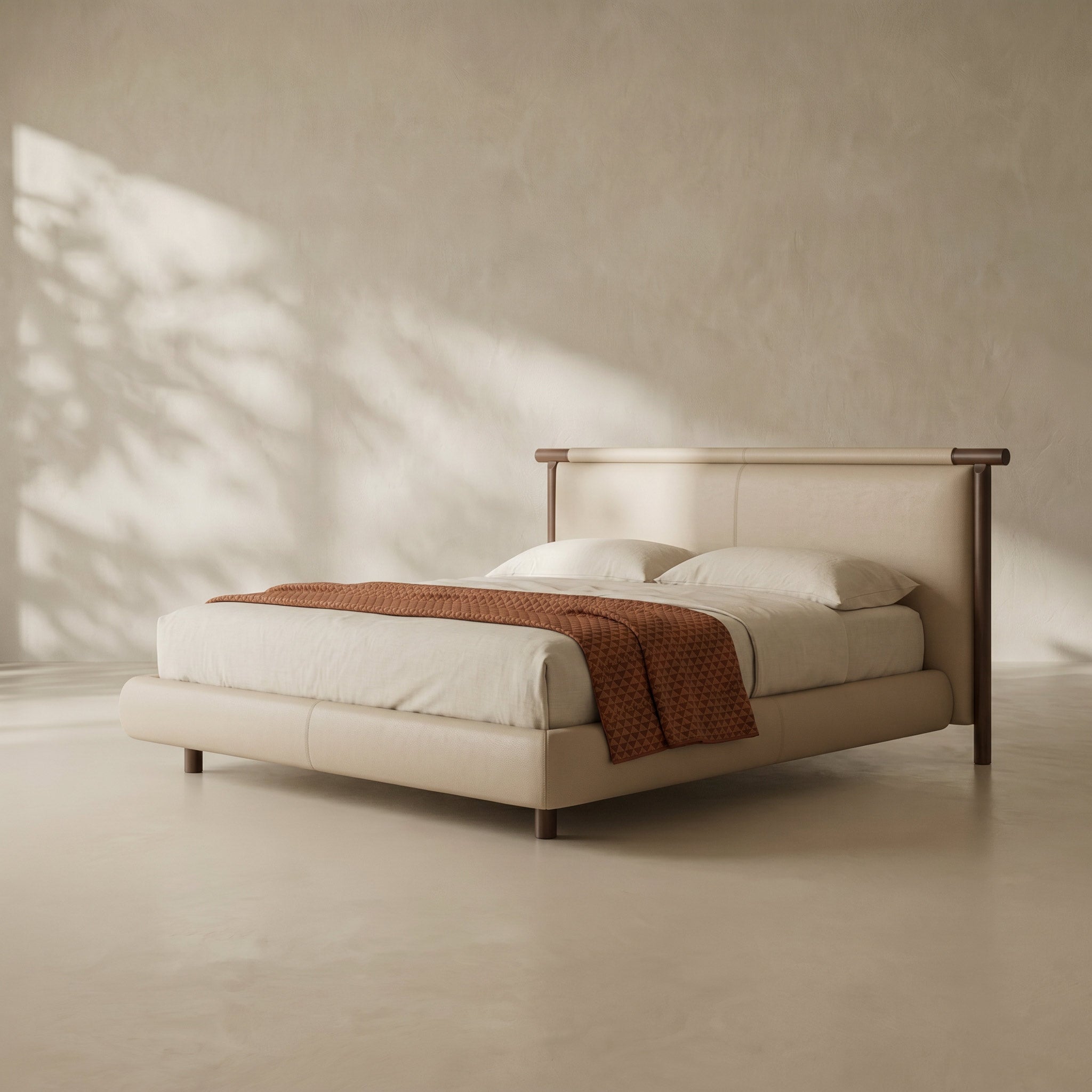 A modern platform bed with a light beige upholstered frame and dark wood headboard and legs, styled with white bedding and a rust-orange textured throw blanket, set against a textured beige wall with soft leaf shadows.