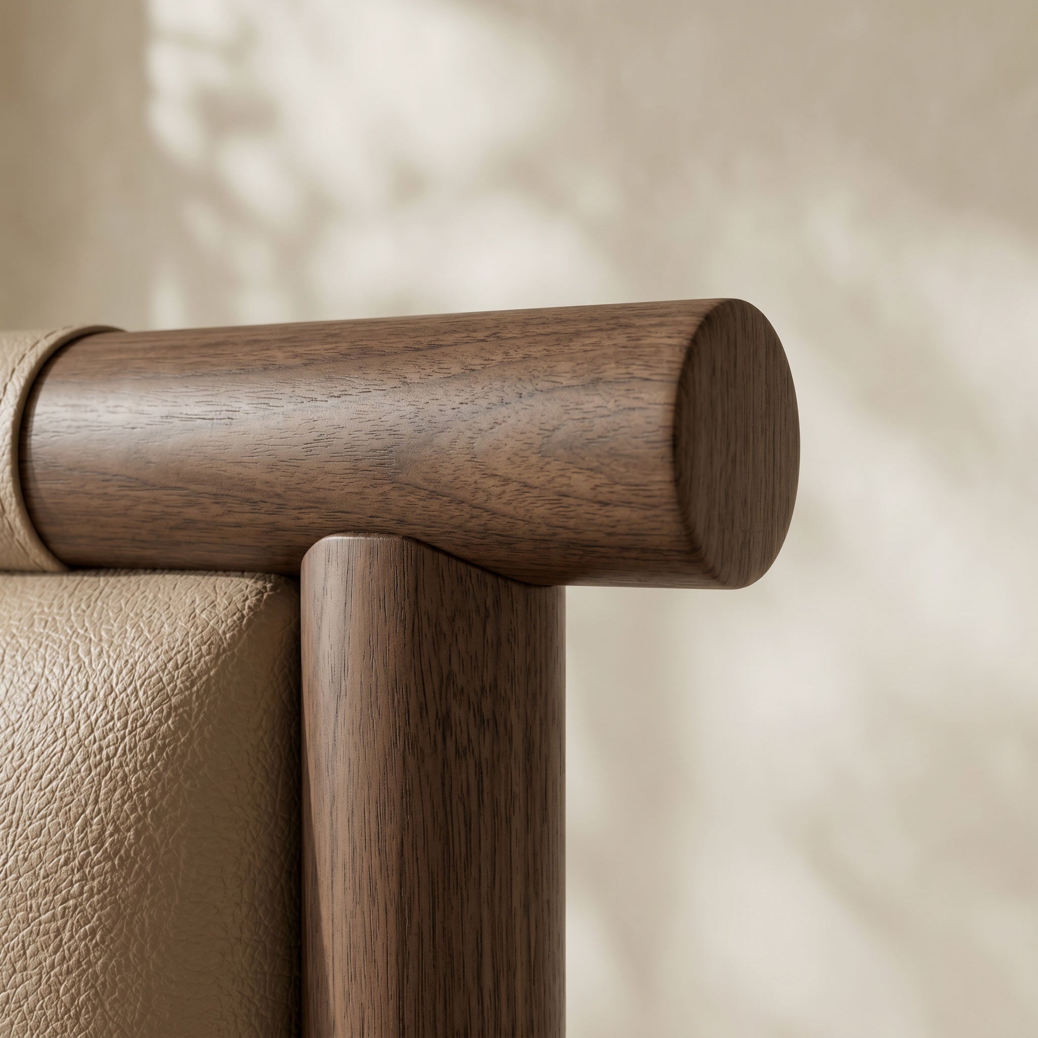 Close-up detail of a wooden chair corner with a dark brown cylindrical armrest and a beige textured leather seat against a softly lit neutral background.