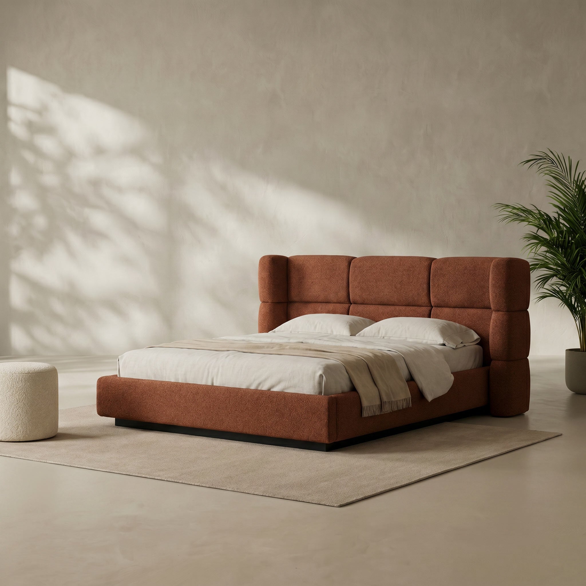 A modern platform bed with a tall, segmented tufted headboard upholstered in rust-orange fabric, styled with white bedding and a beige throw blanket on a light beige rug in a minimalist room.