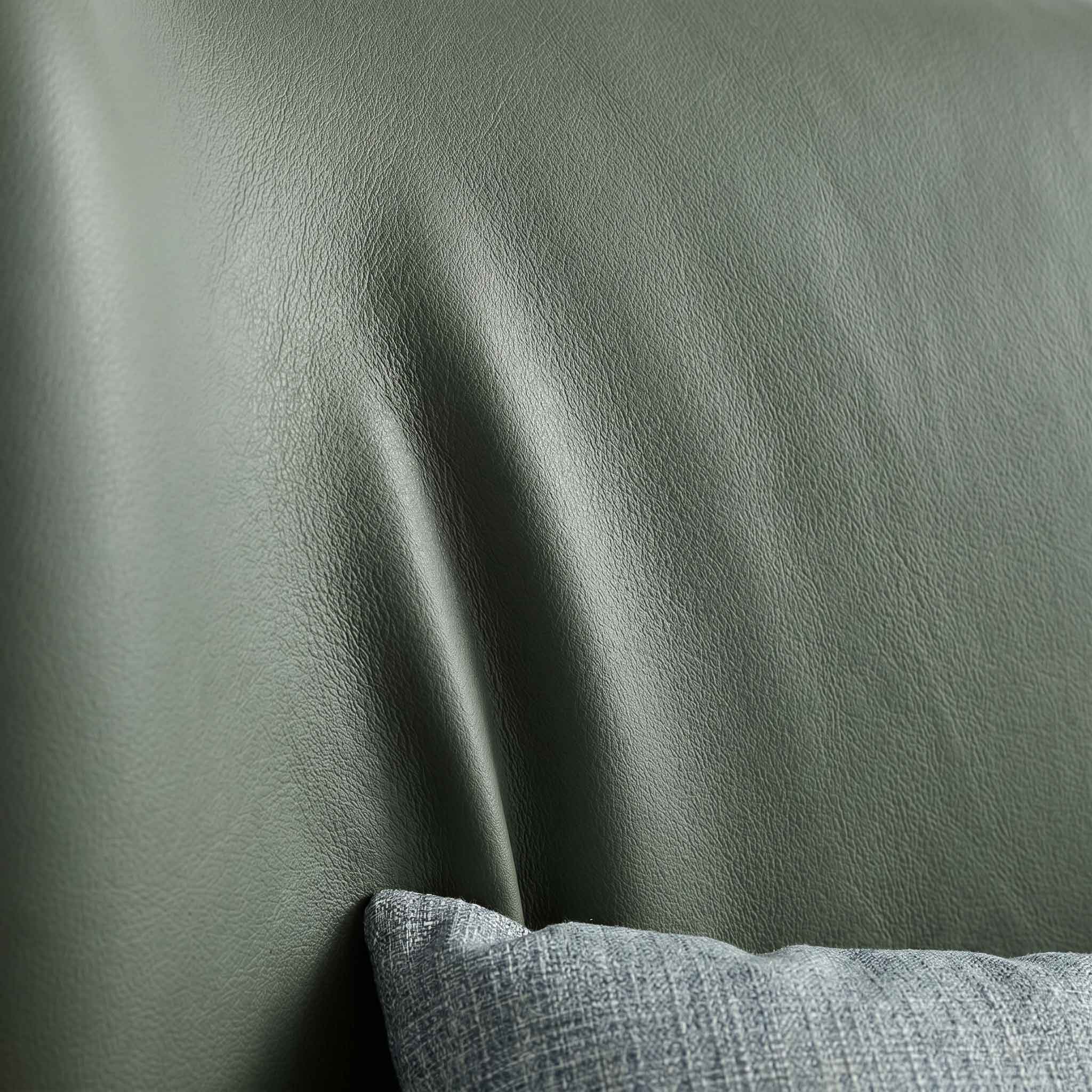 Close-up of a dark sage green leather or faux-leather surface with soft folds and a small portion of a gray textured pillow visible at the bottom.