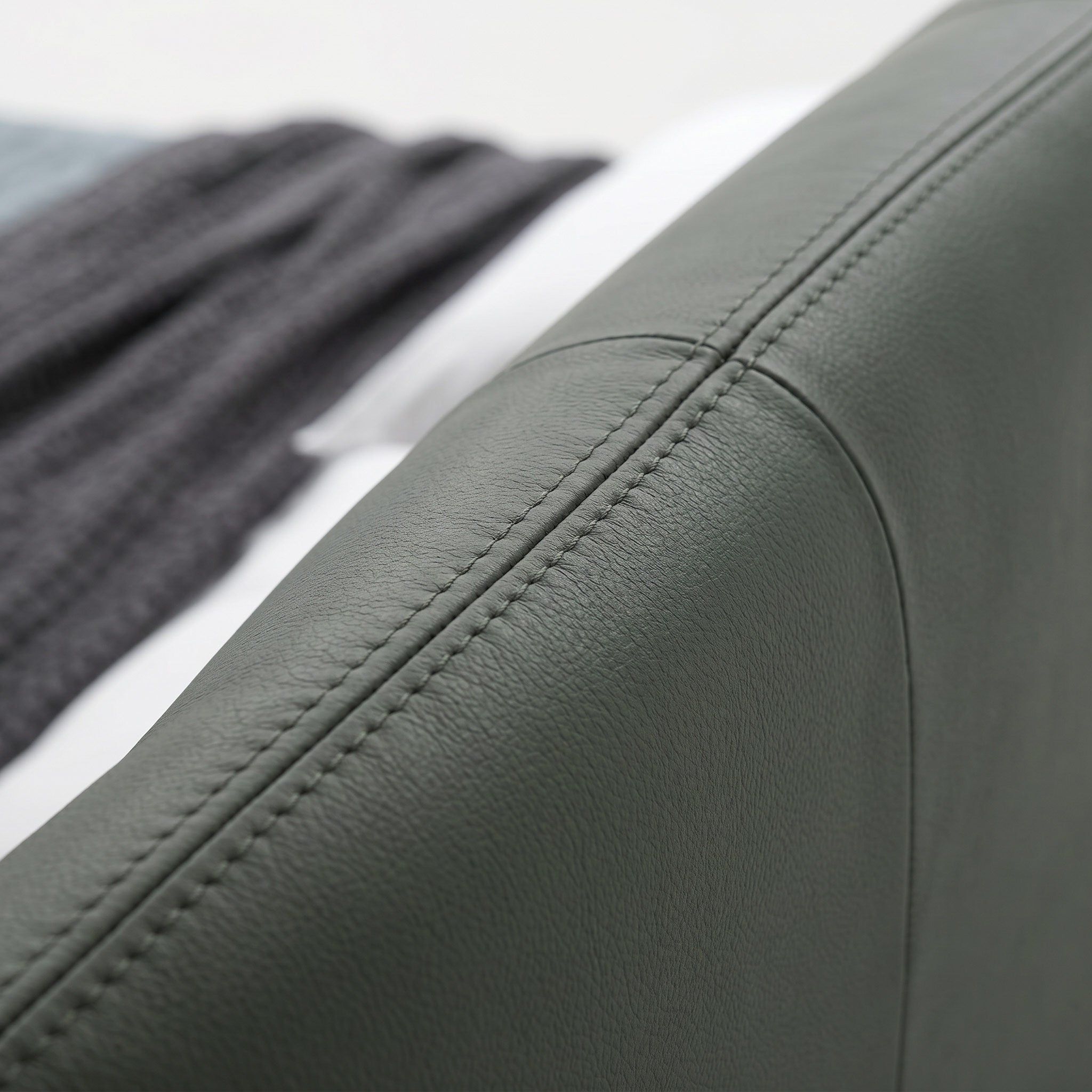 Close-up of a dark gray upholstered arm or cushion with visible stitching, shown against a softly blurred background with a dark knit textile and white surface.