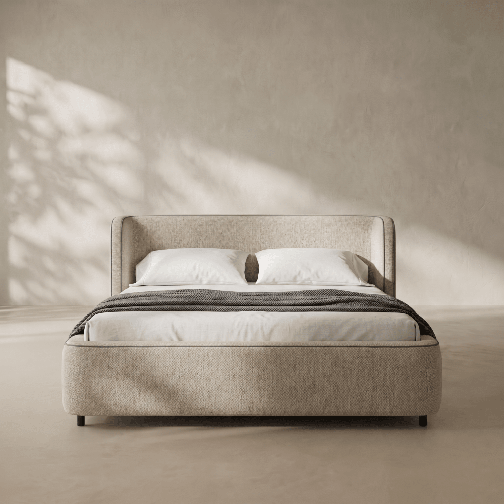 A modern upholstered bed with a low platform frame and tall headboard, shown in a minimalist room with warm sunlight casting leaf shadows on a textured beige wall.