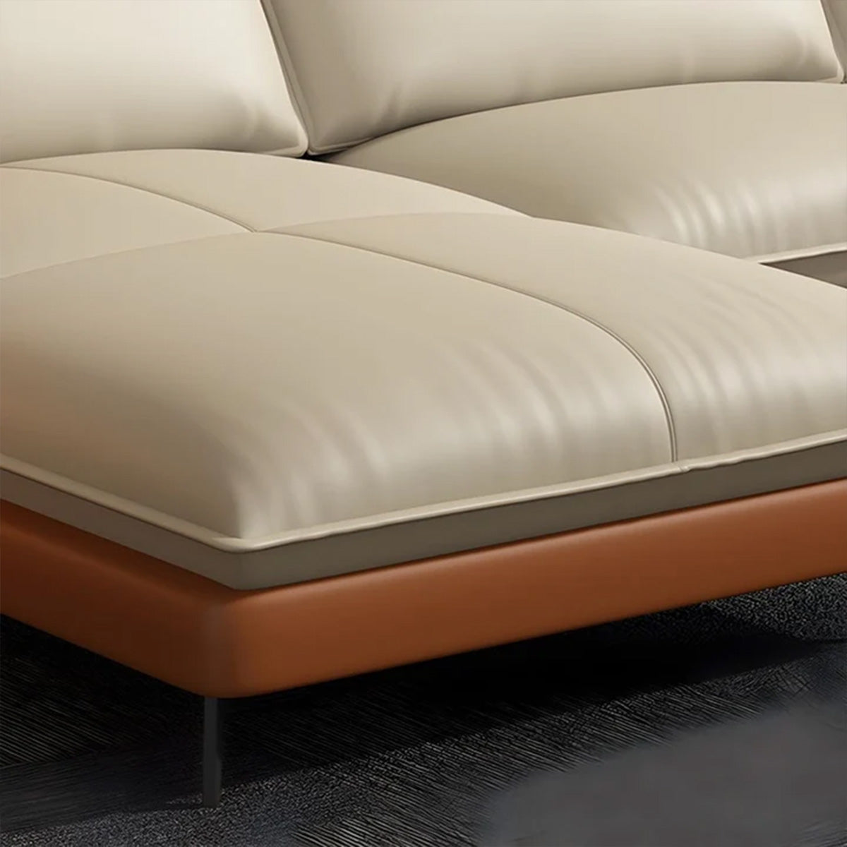 Close-up detail shot of the NOVA sofa cushion, showing the layered design. The top cushion is smooth, light cream leather, resting on a thin gray layer, which is supported by the curved, burnt-orange leather base. A thin black metal leg is visible at the bottom.