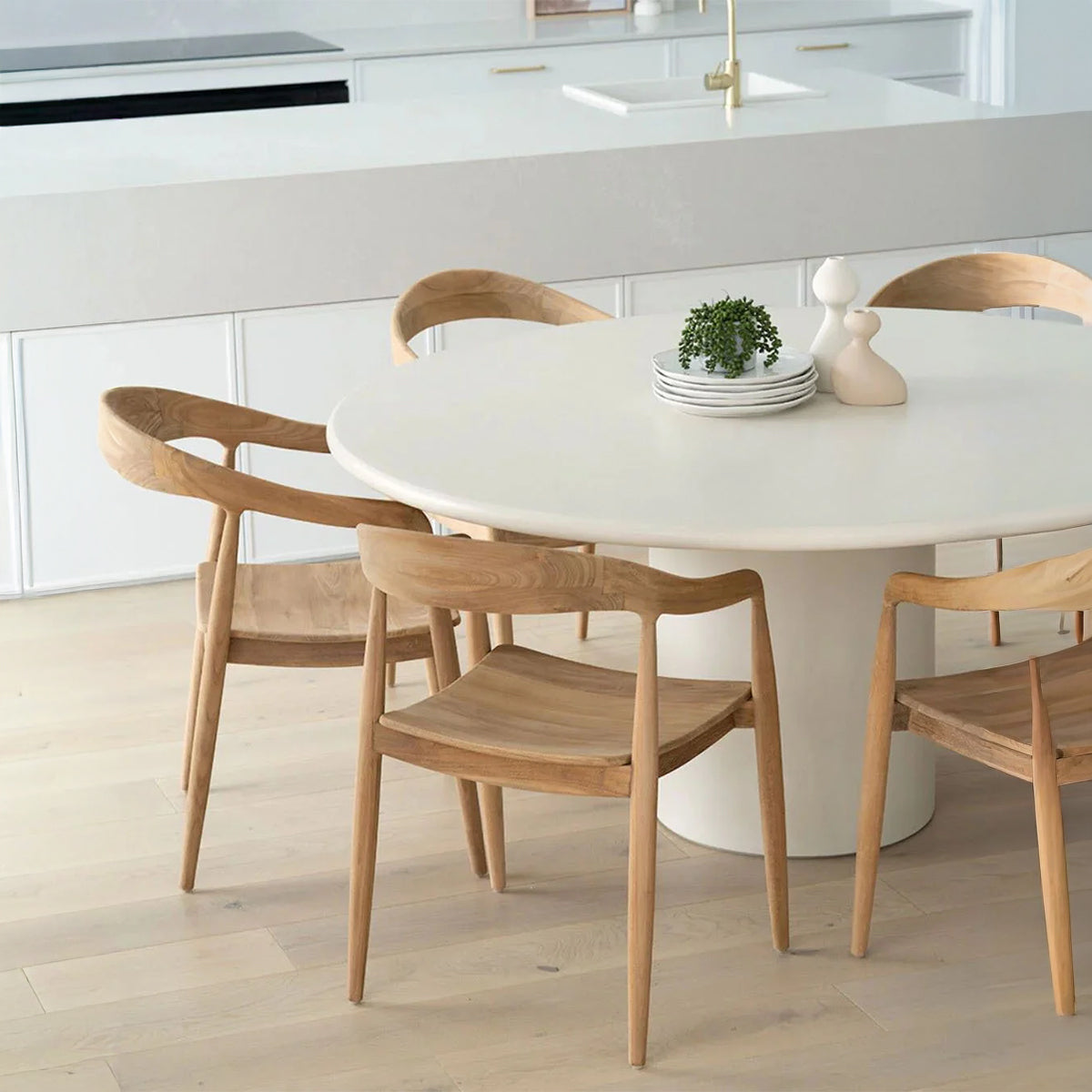 Close-up of wooden dining chairs and white round table with minimalist decor on top.