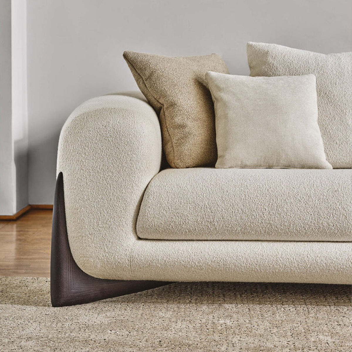 A detailed close-up of the sofa's armrest, showing the texture of the fabric and the curved dark wood foot base.