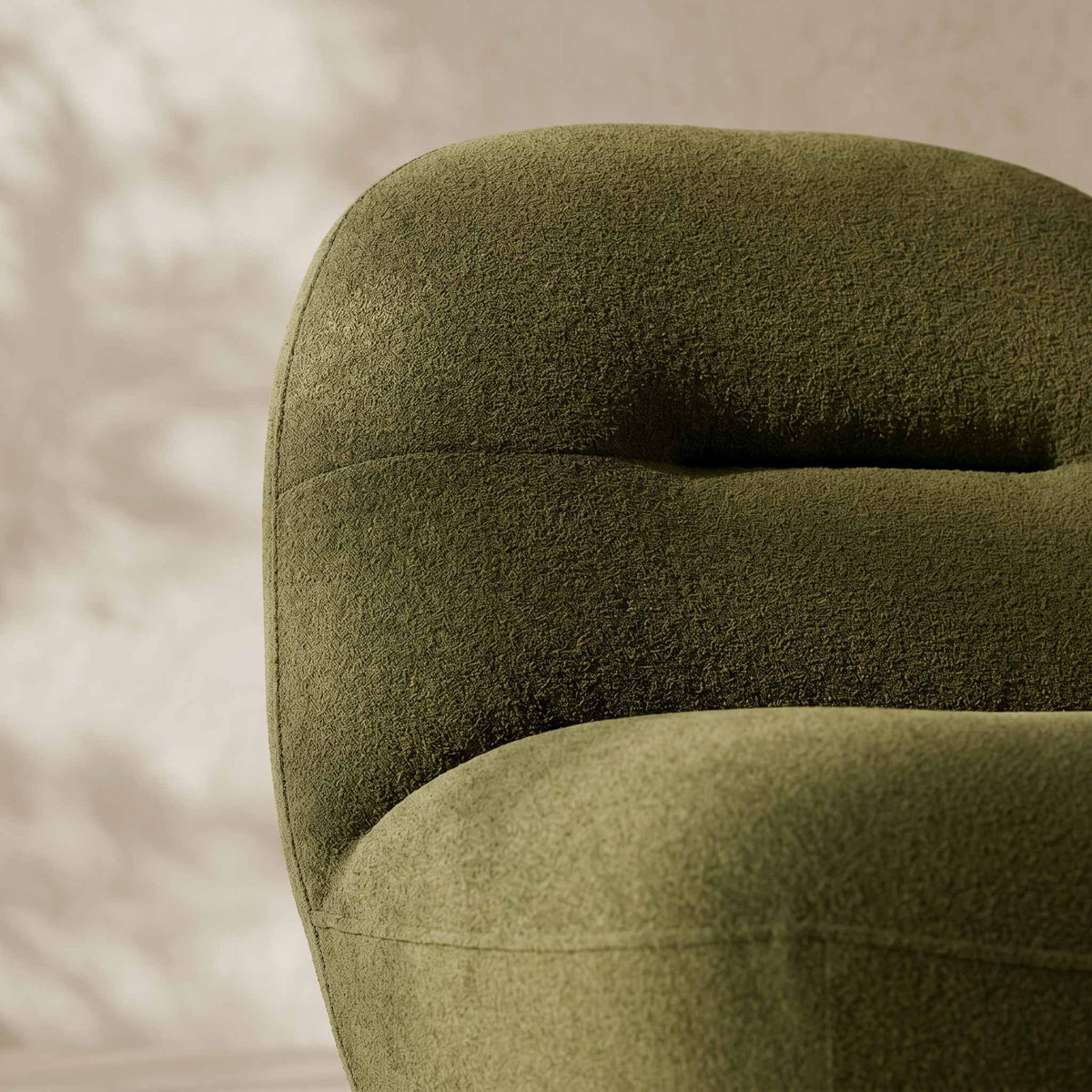 Close-up of a tufted upholstered chair in a textured olive green fabric, showing the curved back and seat against a softly lit neutral background.