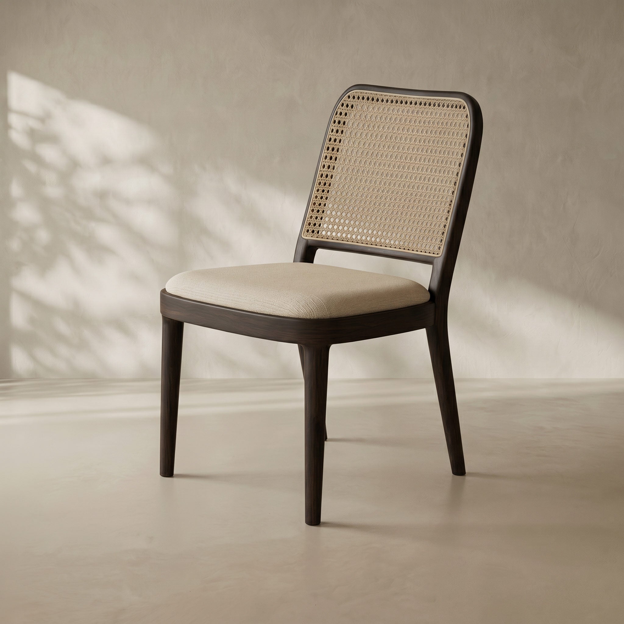 A modern dining chair with a dark brown wooden frame, a beige woven cane backrest, and a light beige upholstered seat cushion, set against a textured beige wall with soft leaf shadows.