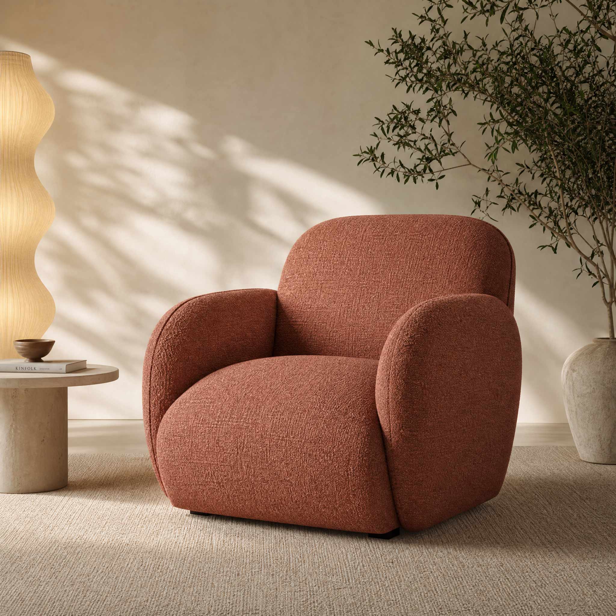 A modern armchair with rounded arms and a textured terracotta fabric, styled in a minimalist room with a wavy floor lamp, a small side table, and a potted plant.