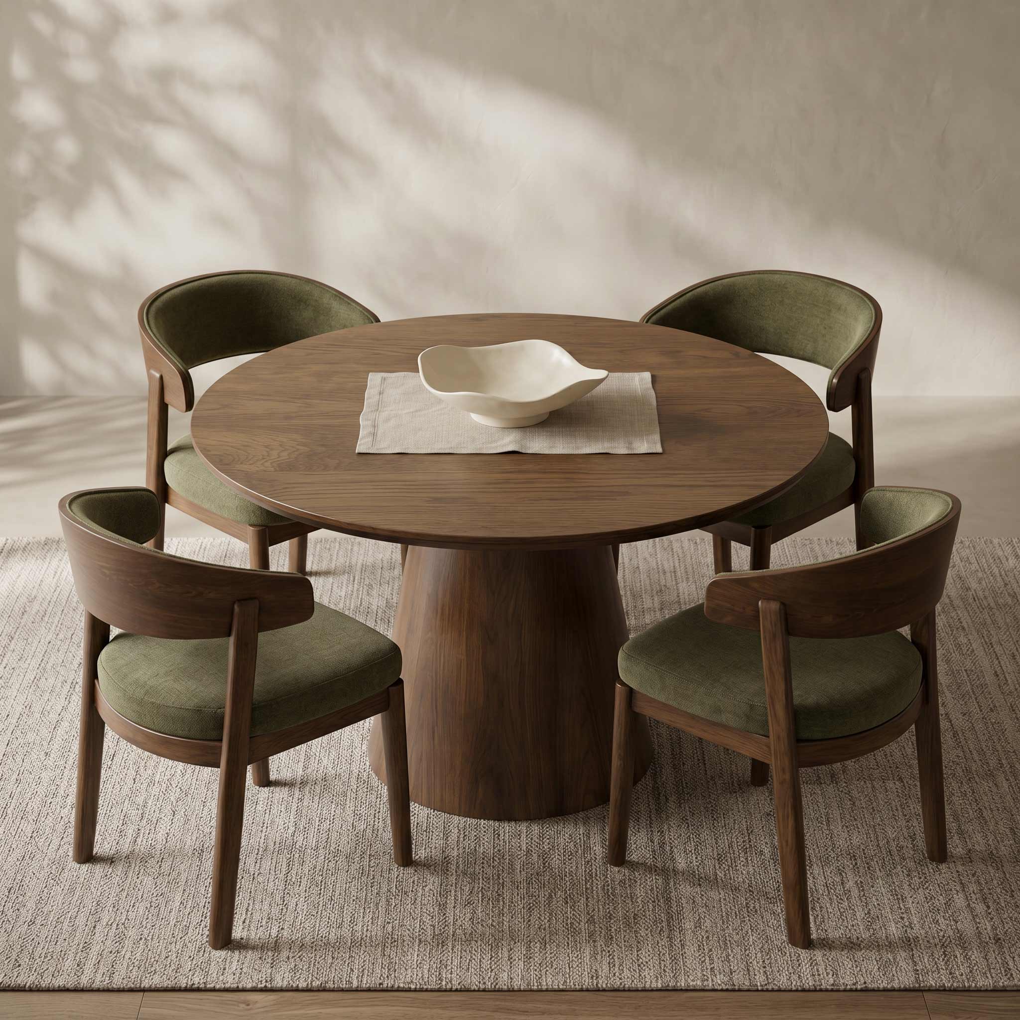 A round wooden dining table with four upholstered chairs in a warm neutral room. The chairs have olive green fabric seats and backs with curved wooden frames.