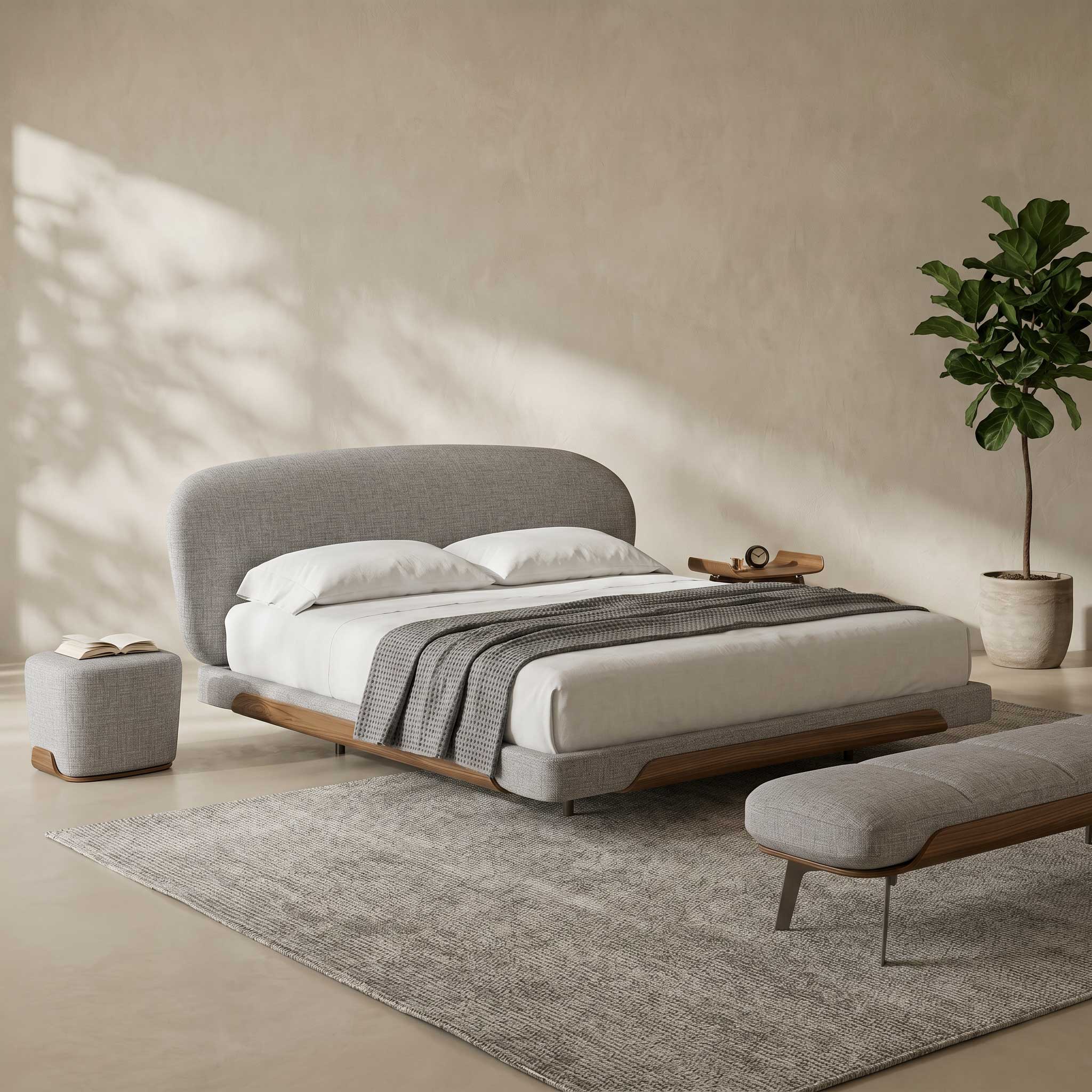 A modern upholstered bed with a curved headboard, white bedding, and a gray throw blanket, styled in a minimalist bedroom with a matching bench, ottoman, rug, and potted plant.