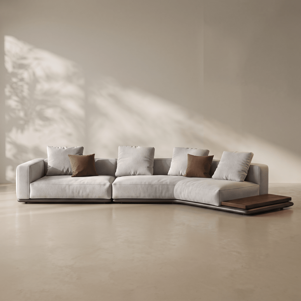 A modern curved sectional sofa in light gray fabric with four brown accent pillows, set in a minimalist beige room with soft diagonal sunlight and shadows.