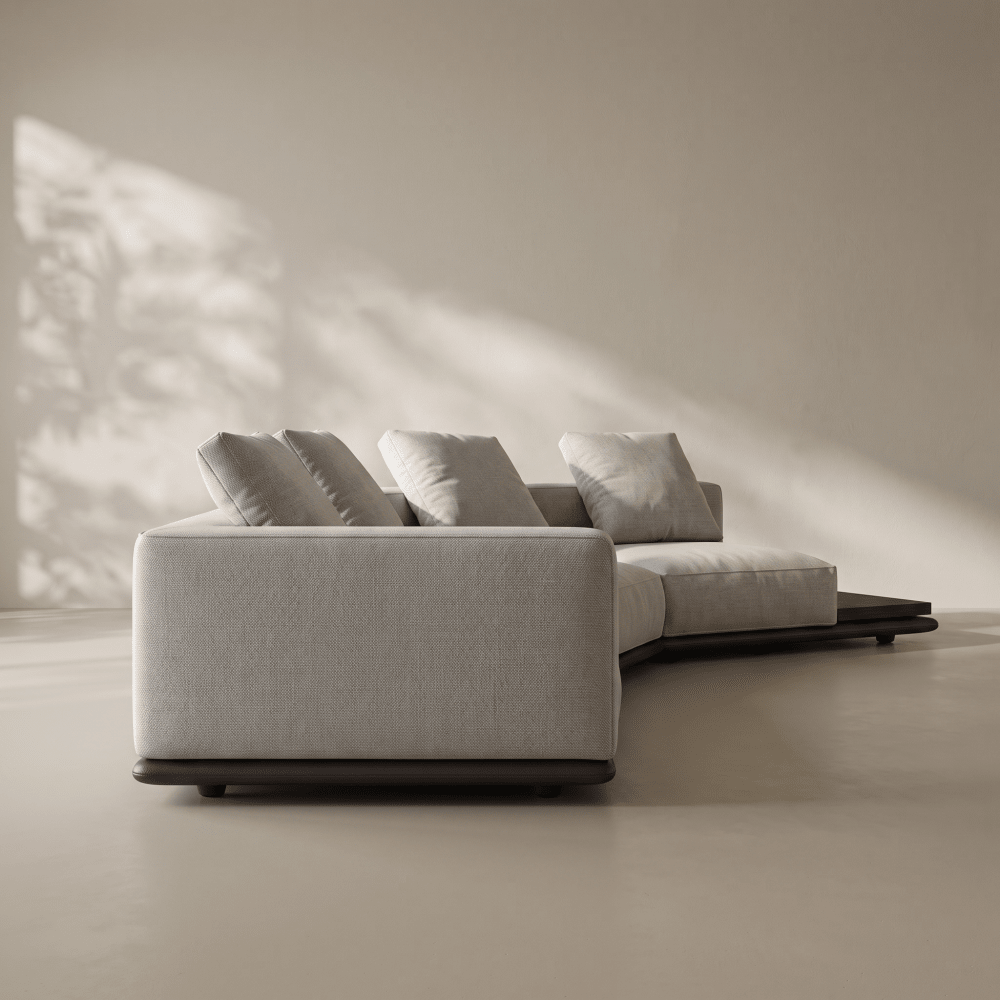 A modern curved sectional sofa in light beige textured fabric with dark wood bases, styled in a minimalist room with warm sunlight and leaf shadows on a neutral beige wall.