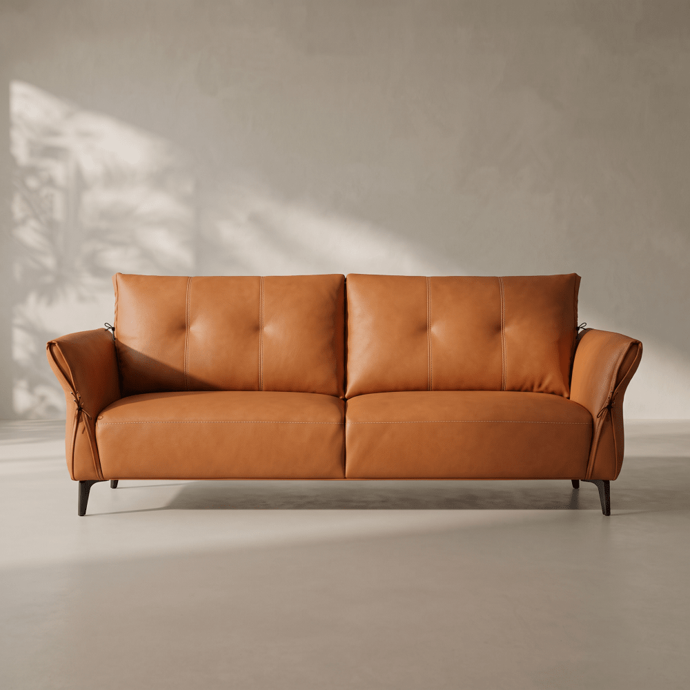 A modern two-seater sofa in warm tan leather with tufted back cushions and dark tapered legs, photographed in a minimalist interior with soft sunlight and shadow on a textured wall.