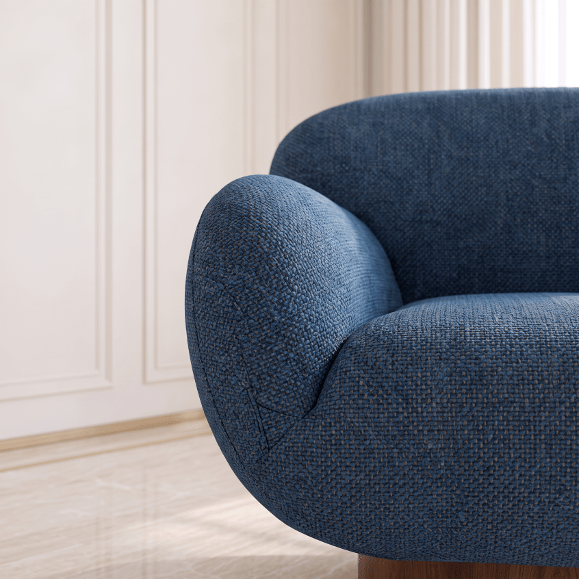 A close-up of a modern blue textured fabric armchair in a bright, elegant room with cream paneled walls and light wood flooring.