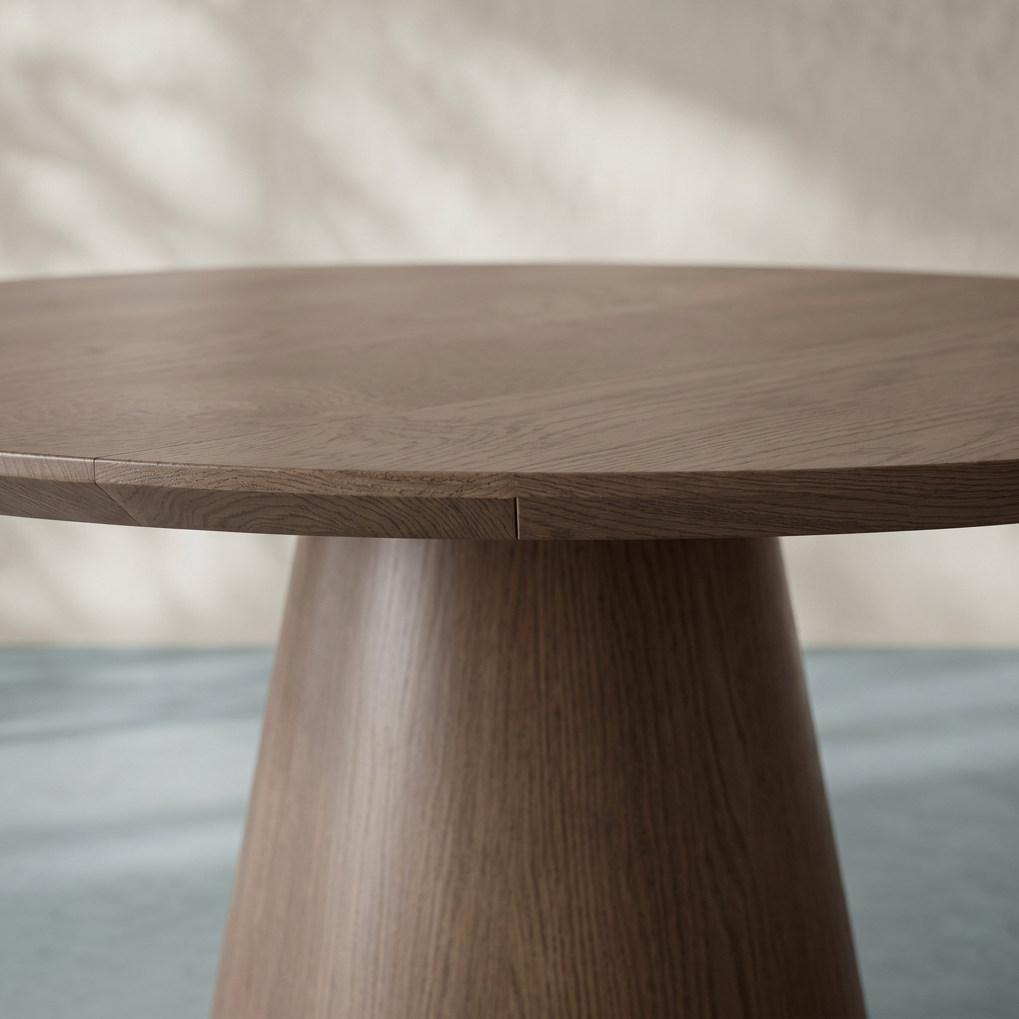 A close-up of a round wooden dining table with a tapered pedestal base, showcasing the natural wood grain and finish.