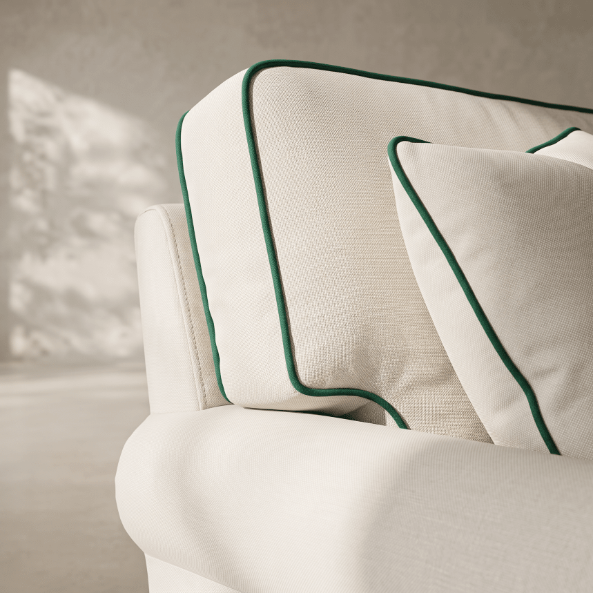 Close-up of a white upholstered armchair with two matching throw pillows featuring dark green piping, set against a softly lit neutral interior background.