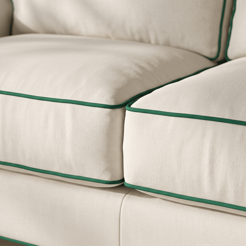 Close-up of cream-colored upholstered cushions with dark green piping trim, showing the fabric texture and clean edges.