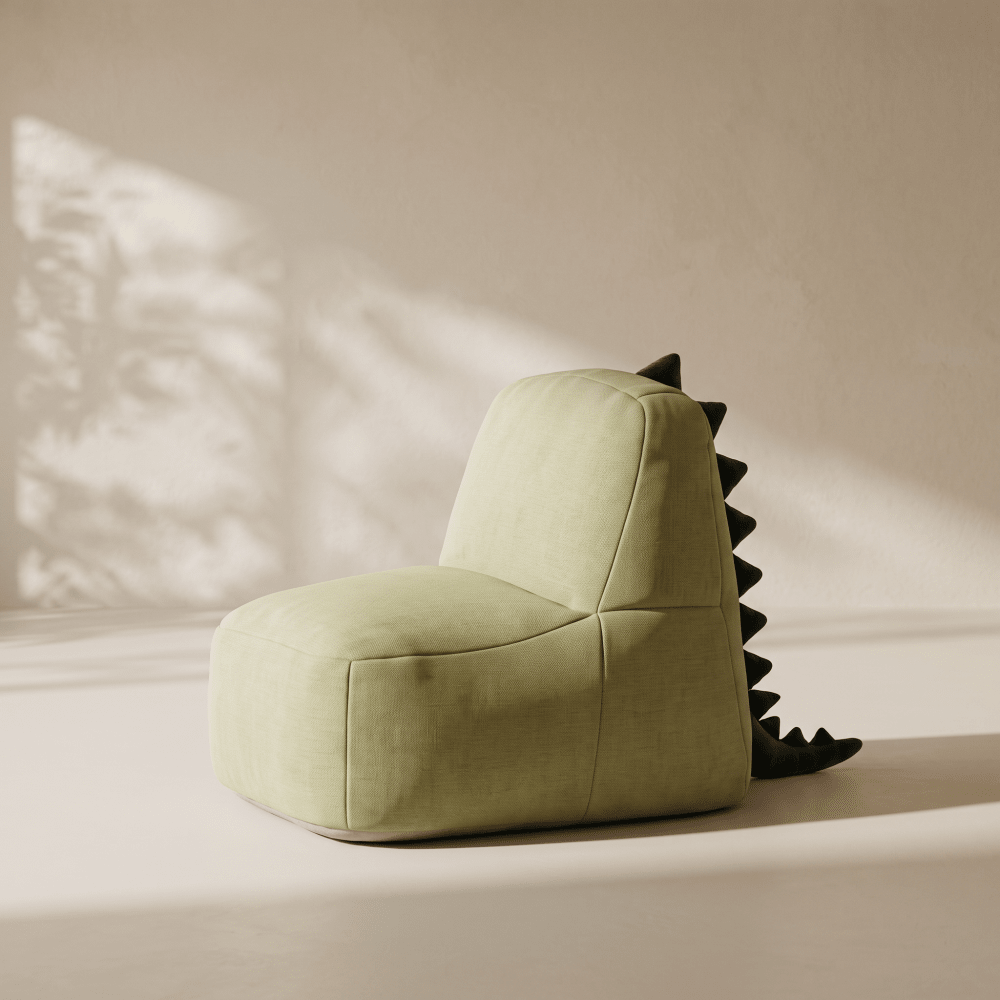 A light sage green dinosaur-themed bean bag chair with black spikes along the back, set against a warm beige wall with soft leaf shadows.