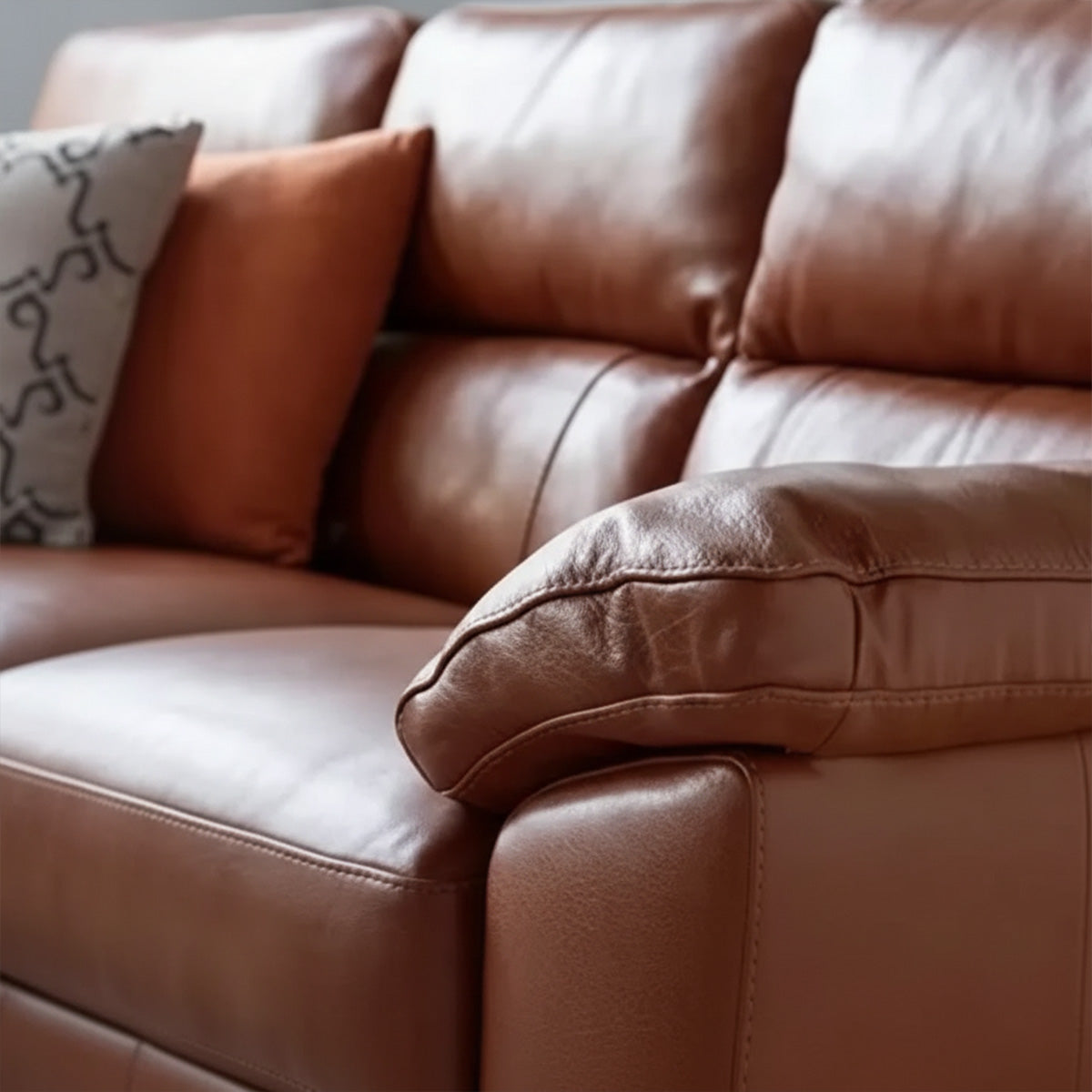 A close-up shot focusing on the plush, rolled armrest of the brown leather sofa, highlighting the texture and stitching detail. A few throw pillows are partially visible.