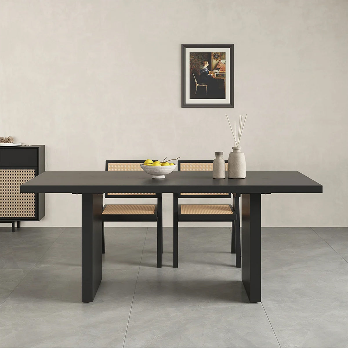 Frontal view of sleek black dining table with two cane chairs, showcasing design against a light wall with framed art.