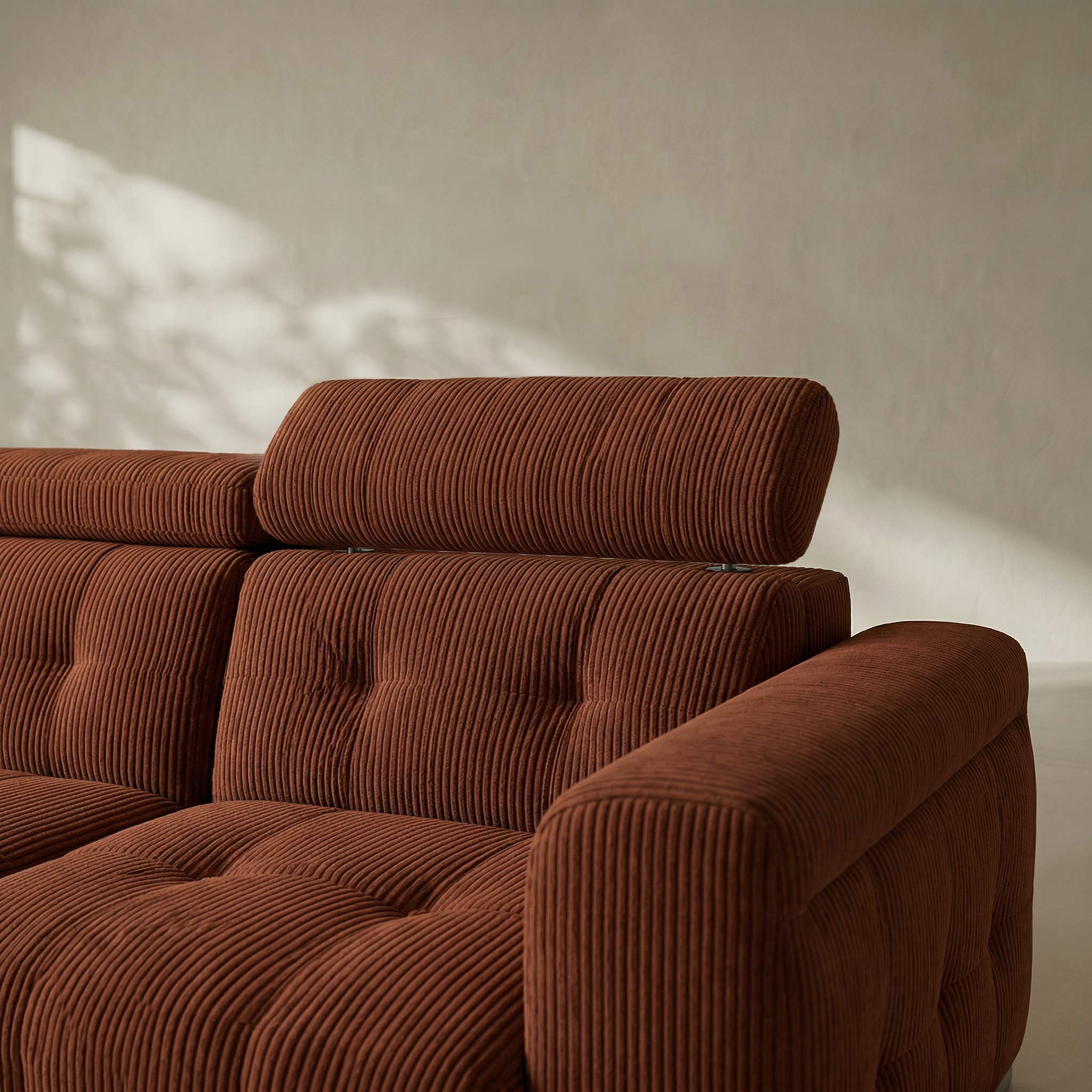 Brown corduroy sofa against a beige wall with soft shadows.