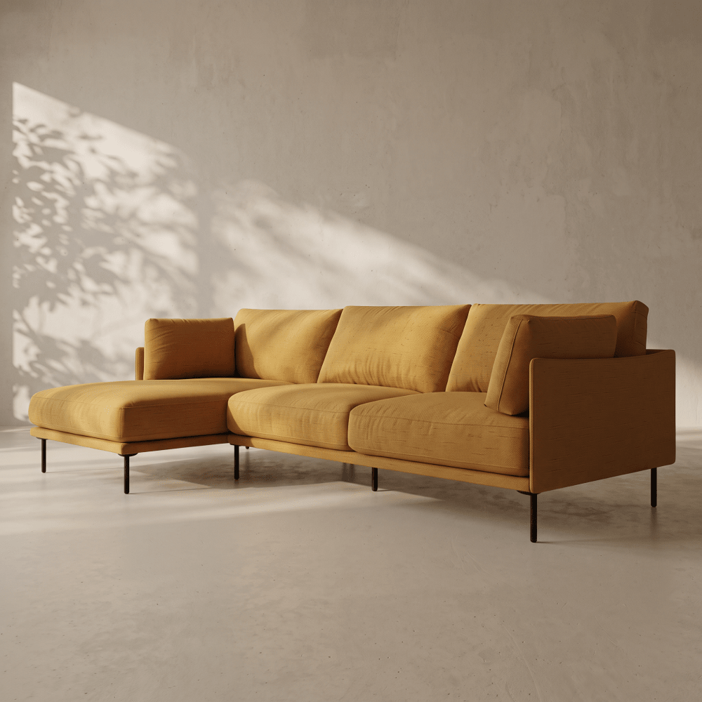 A modern sectional sofa upholstered in a warm mustard-yellow fabric, featuring a left-facing chaise and slim black metal legs, set against a textured concrete wall with soft leaf shadows.