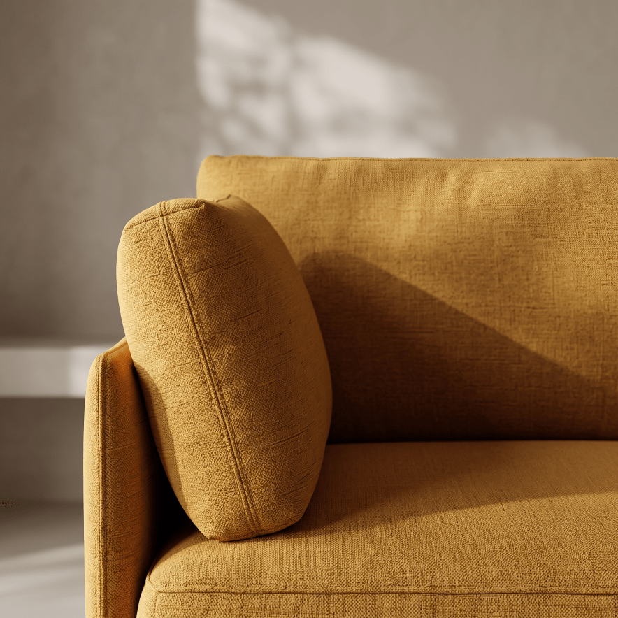 A close-up of a mustard yellow fabric sofa with a matching back cushion, shown in warm natural light against a neutral gray wall.