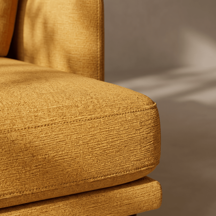 Close-up of a mustard yellow textured fabric sofa cushion with a matching armrest, photographed in warm natural light against a neutral gray background.