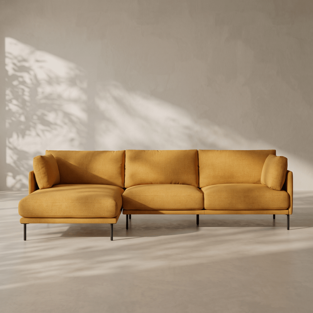 A mustard yellow fabric sectional sofa with a chaise lounge on a minimalist concrete floor against a textured wall with soft leaf shadows.