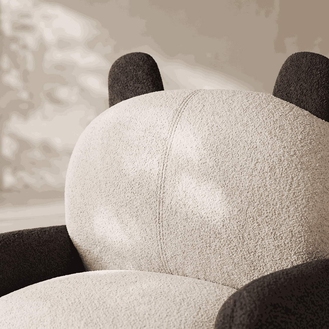 A close-up of a plush armchair with a rounded, bear-like silhouette. The chair features a textured off-white seat and back cushion with dark charcoal gray armrests and ear-like details on top.