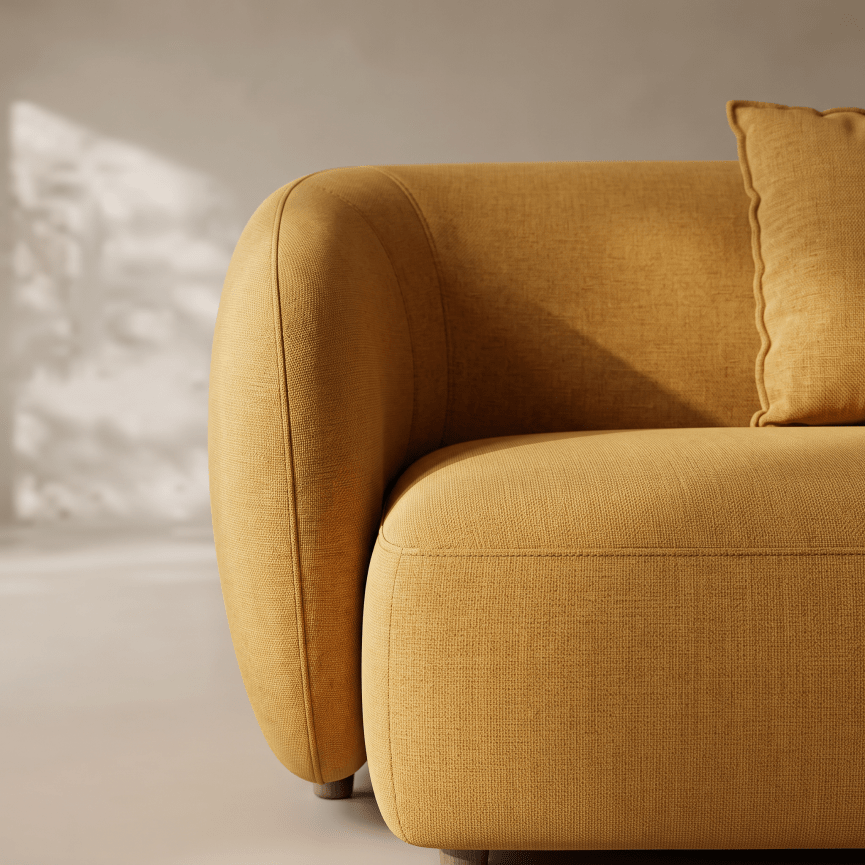 A close-up of a mustard yellow fabric sofa with a matching throw pillow, showing the textured upholstery and rounded armrest in a softly lit interior setting.