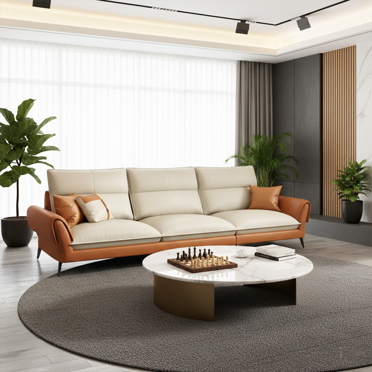 A three-seater NOVA sofa featuring tan leather trim and cream cushions, placed in a modern living room setting. A round white marble coffee table with a chess set is centered in front of the sofa, which is sitting on a large round gray rug. Natural light streams in from a large window behind the sofa.