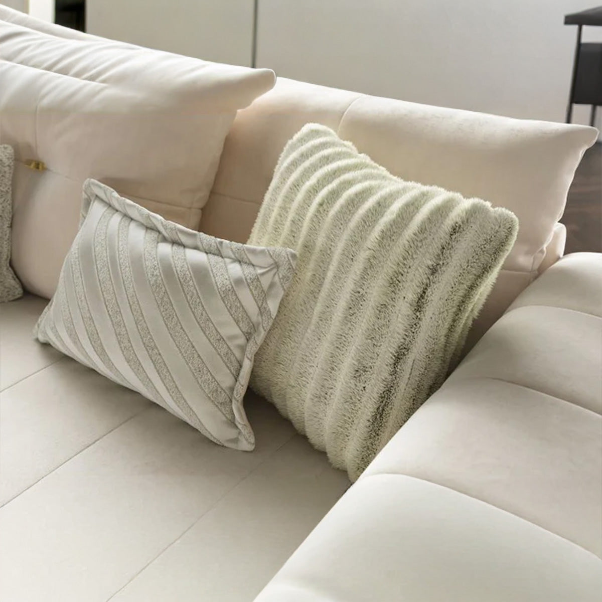 Close-up of textured scatter cushions on Alcotta sofa, featuring striped and ribbed faux fur designs in matching cream tones.