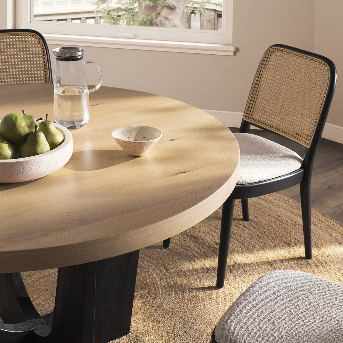 Close-up view of a modern wooden round dining table with rattan chair and minimalist table decor.