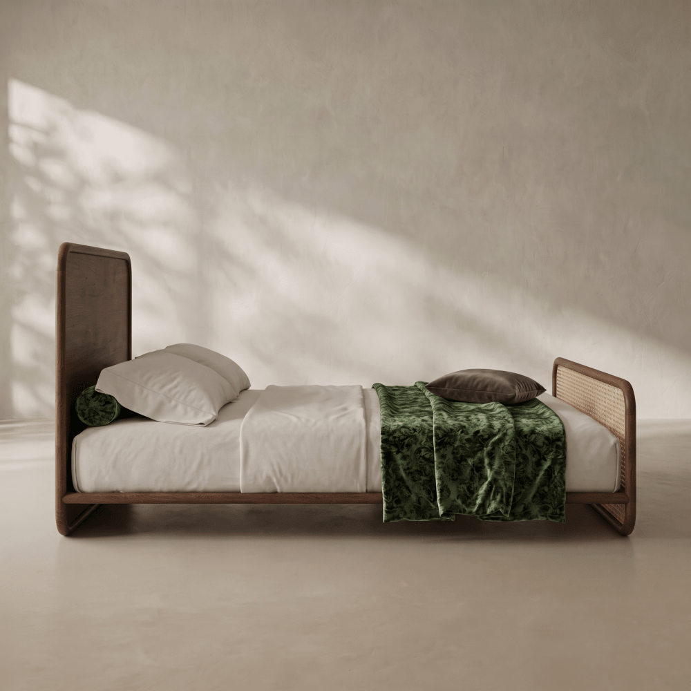 A minimalist wooden bed frame with a tall headboard and low footboard, styled with white bedding and a green velvet throw blanket in a warm, sunlit room.