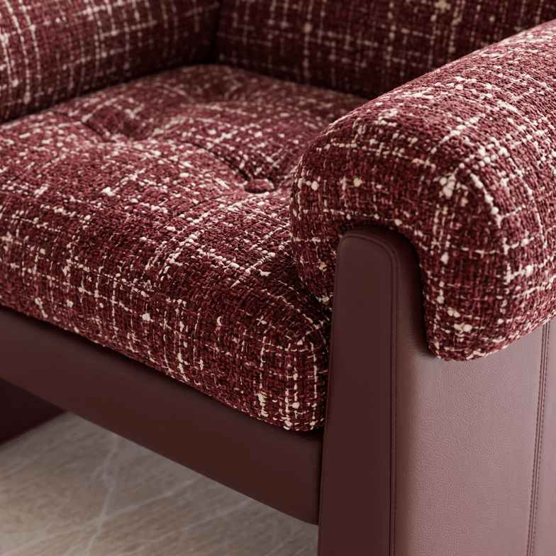 Close-up of a tufted upholstered armchair corner with deep burgundy and cream woven fabric cushions and a dark brown frame.