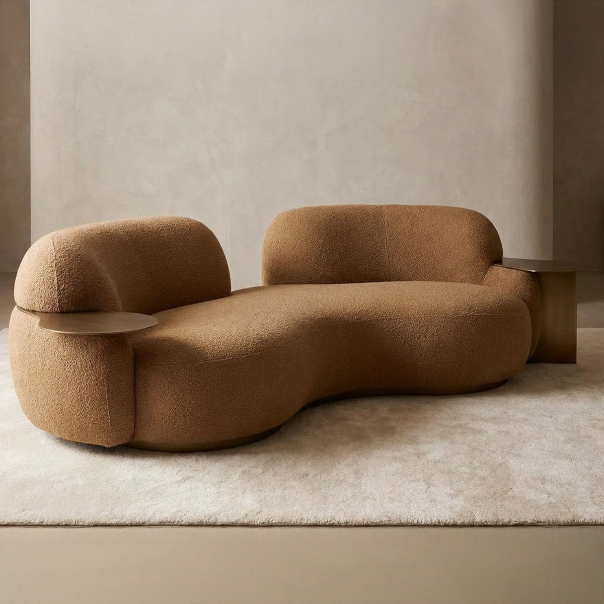 Two-seater curved loveseat in caramel bouclé with a kidney-bean shape, featuring a built-in brass side table and a matching metallic base in a minimalist setting.