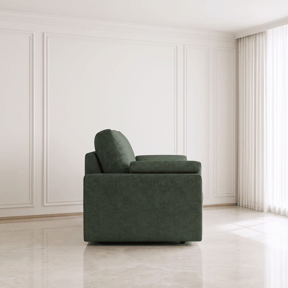 A modern dark green upholstered armchair with a square base and rounded back cushion, positioned in a minimalist room with white paneled walls and light-colored flooring.
