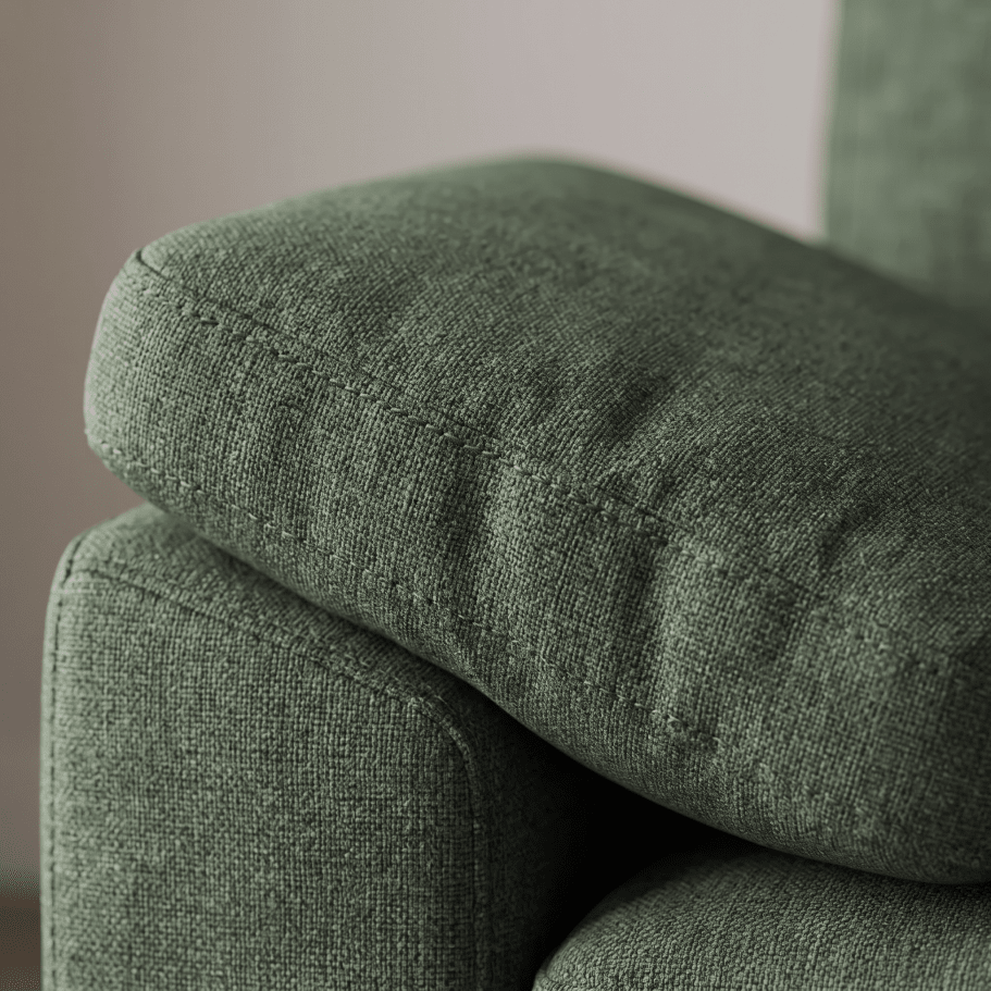 Close-up of a textured sage green fabric armchair cushion resting on the armrest of the same chair.