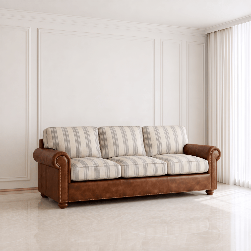 A three-seat sofa with brown leather arms and base, and cream and beige striped cushions, set in a bright, modern room with white paneled walls and a window with sheer curtains.