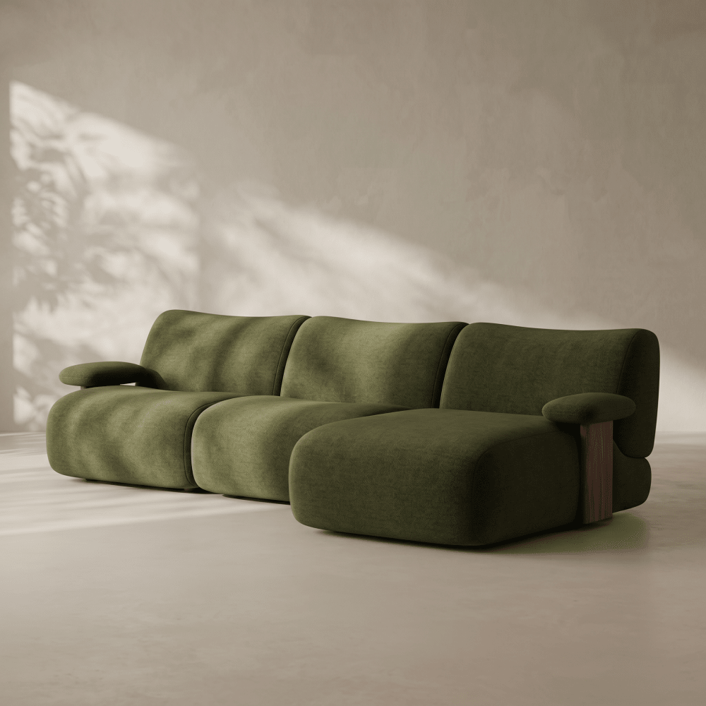 A modern modular sectional sofa upholstered in olive green fabric, featuring rounded blocky cushions and a dark wood accent leg, set against a textured beige wall with soft leafy shadows.