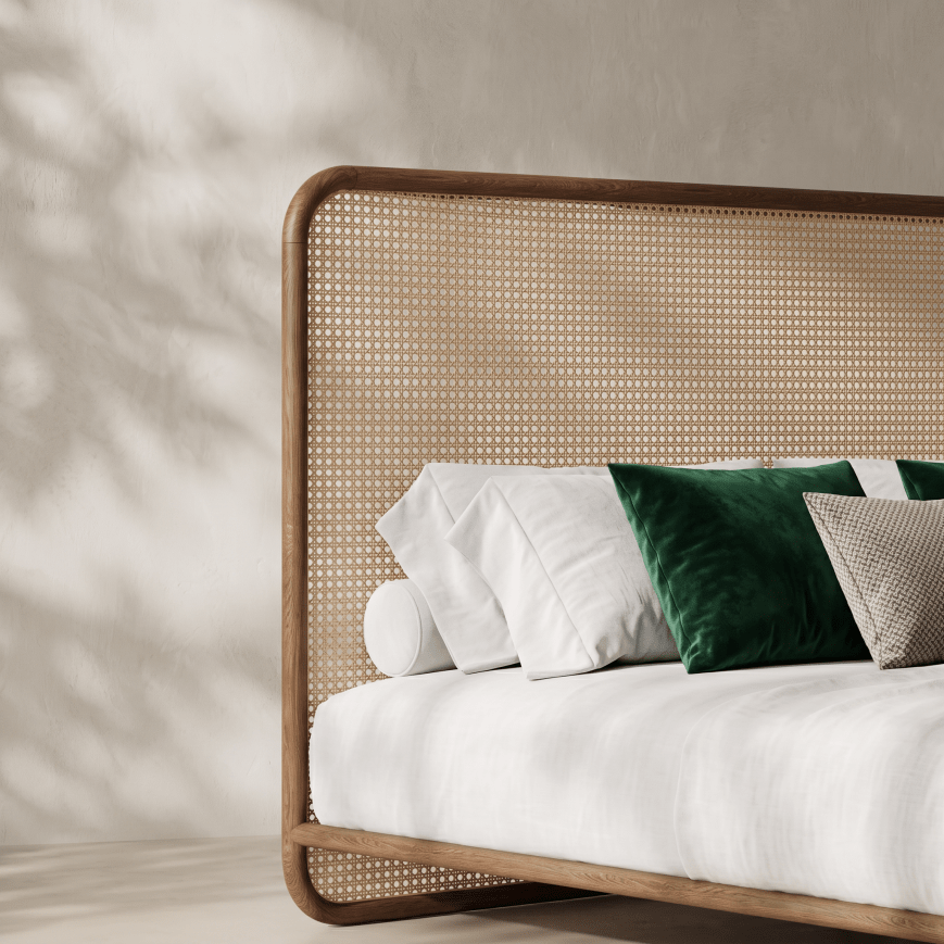 A modern low-profile platform bed with a curved wooden frame and woven cane headboard, styled with white bedding and green and beige accent pillows against a textured beige wall with soft leaf shadows.