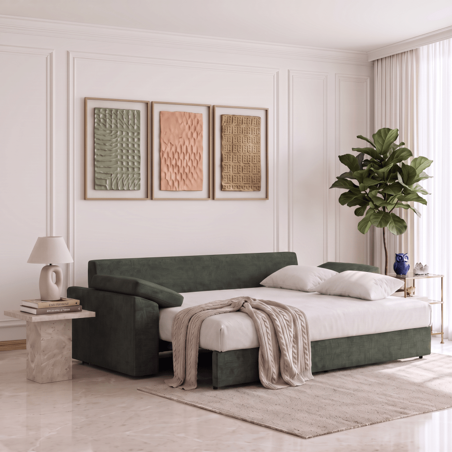 A dark green upholstered daybed or sofa bed with white bedding and pillows, styled in a bright, modern room with a marble side table, lamp, framed wall art, and a potted plant.