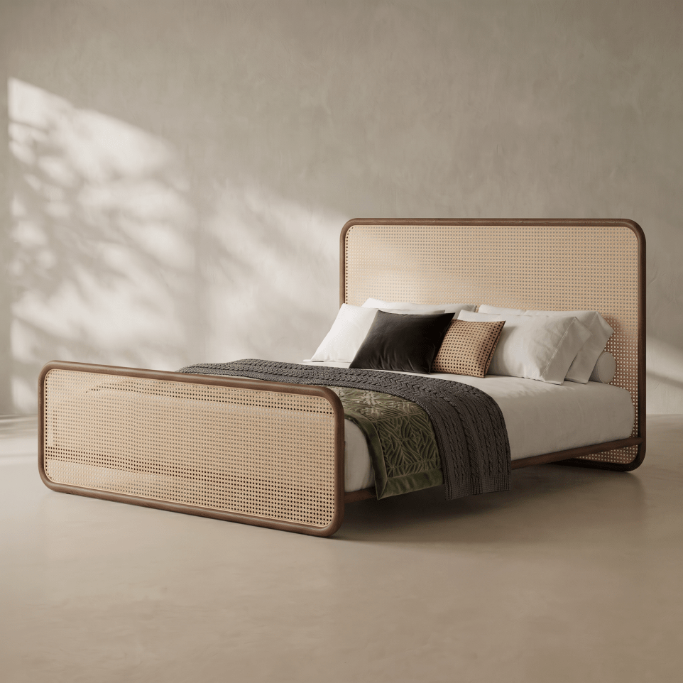 A modern platform bed with a natural cane headboard and footboard, styled with white bedding, a dark gray throw blanket, and accent pillows in a minimalist room with textured plaster walls and soft leaf shadows.