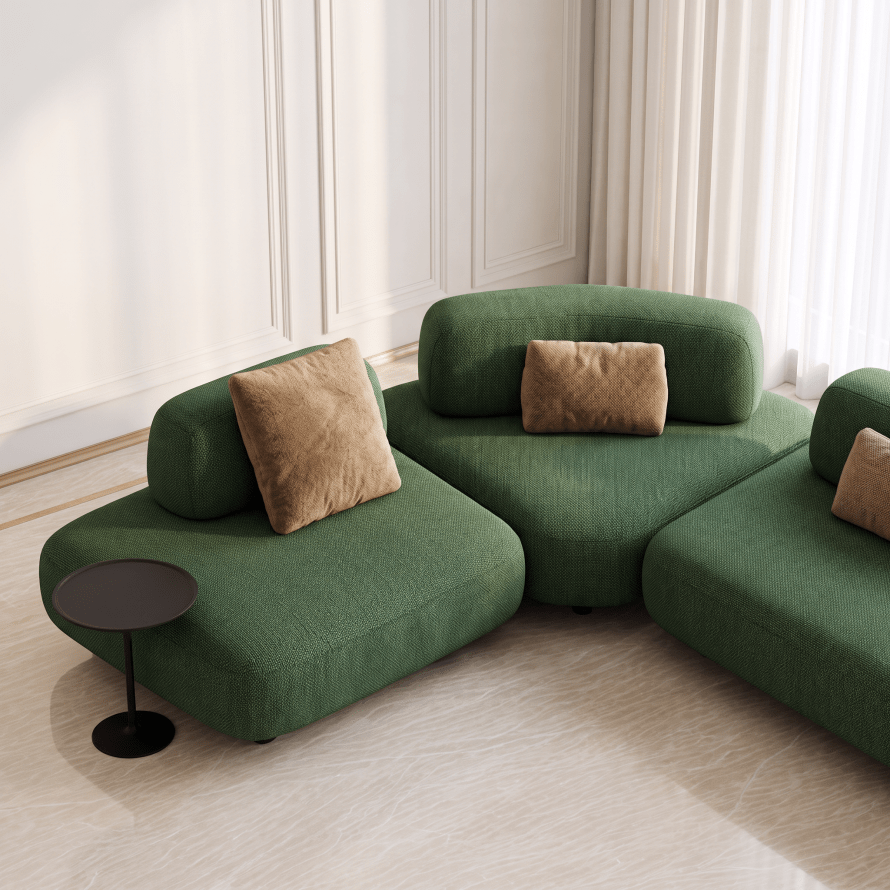 A modern modular sectional sofa in textured olive green fabric with two tan throw pillows, styled in a bright, minimalist living room with cream walls and light wood flooring.