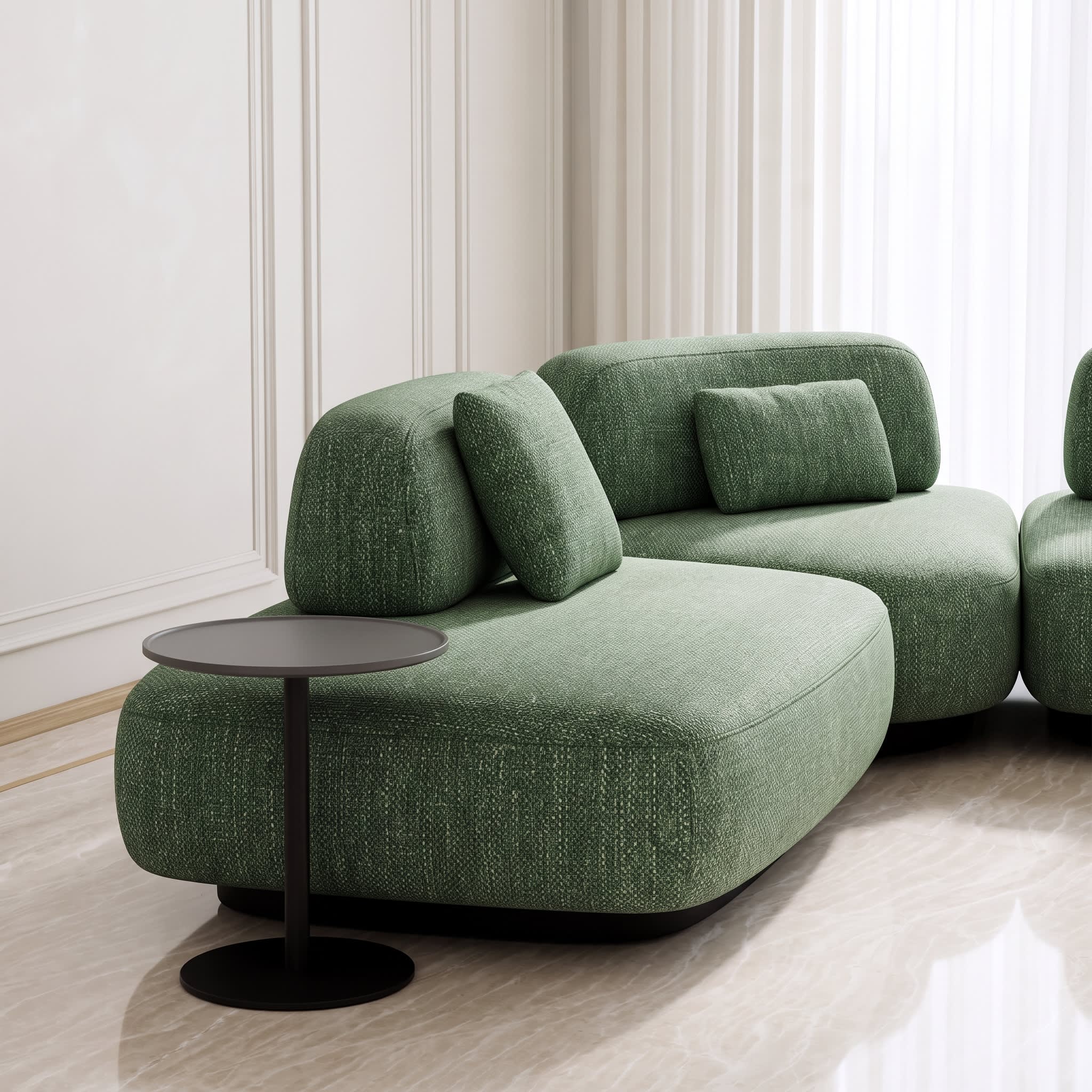 A modern modular sofa upholstered in textured sage green fabric, styled in a minimalist room with a small round black side table and light-colored flooring.