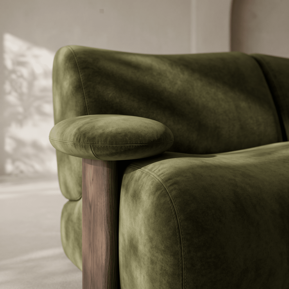 Close-up of an olive green velvet sofa with a rounded armrest and a dark wood leg in a softly lit interior setting.