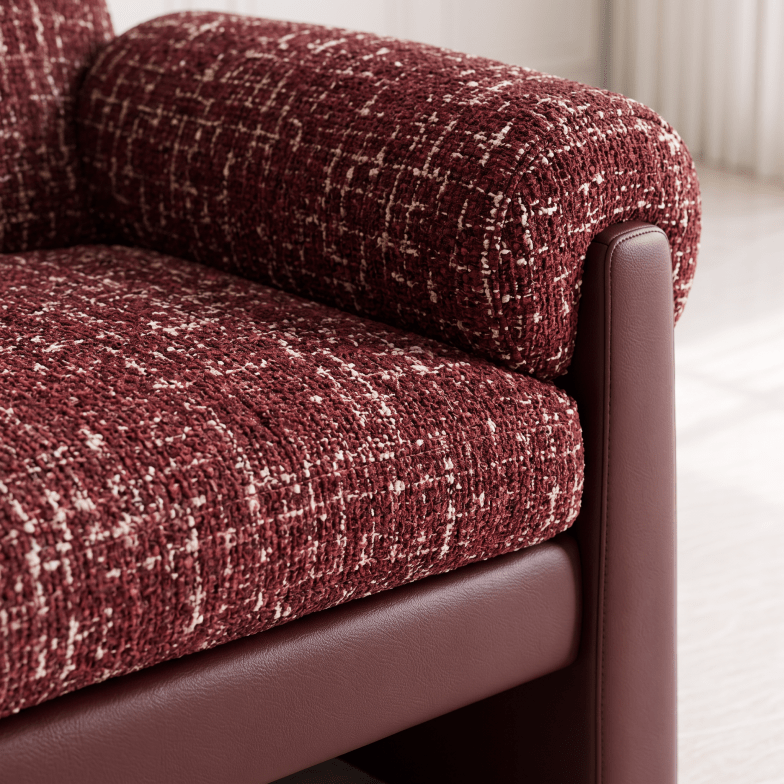 Close-up of a sofa upholstered in a textured burgundy and cream woven fabric, with a smooth dark brown side panel and matching base, shown in a bright interior setting.